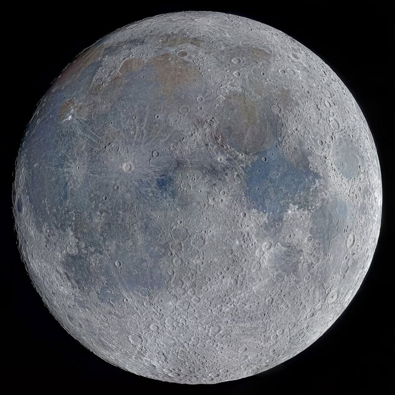Detailed close-up image of the full moon, showing its craters, maria, and surface textures in shades of gray, with subtle hints of blue and brown under bright illumination against a black background.