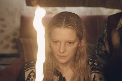 A scene from Starve Acre. Close-up of a woman staring at a flame. 