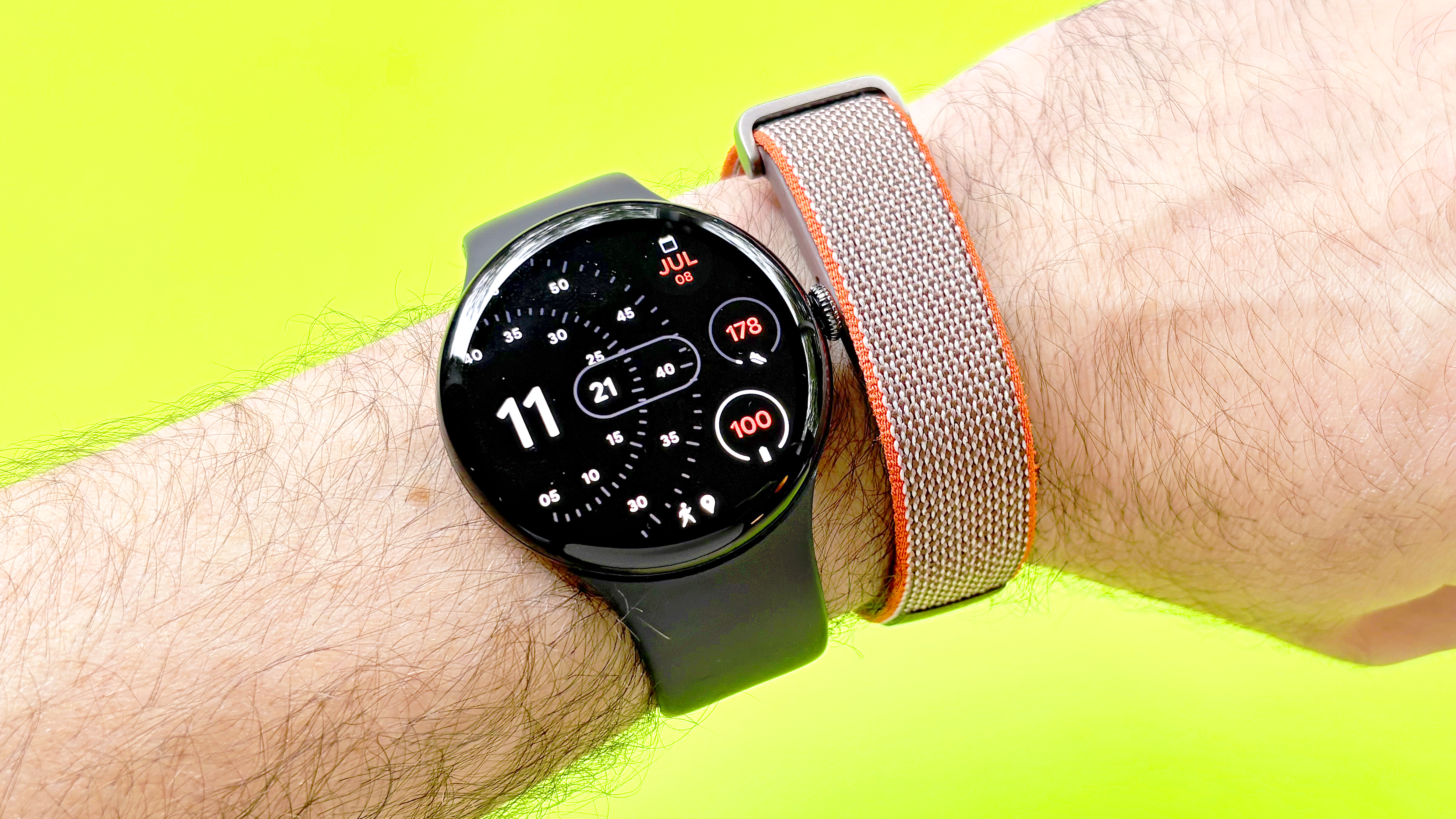 Close-up of the Google Pixel Watch 4 and Fitbit Air on a user's wrist against a yellow/green background