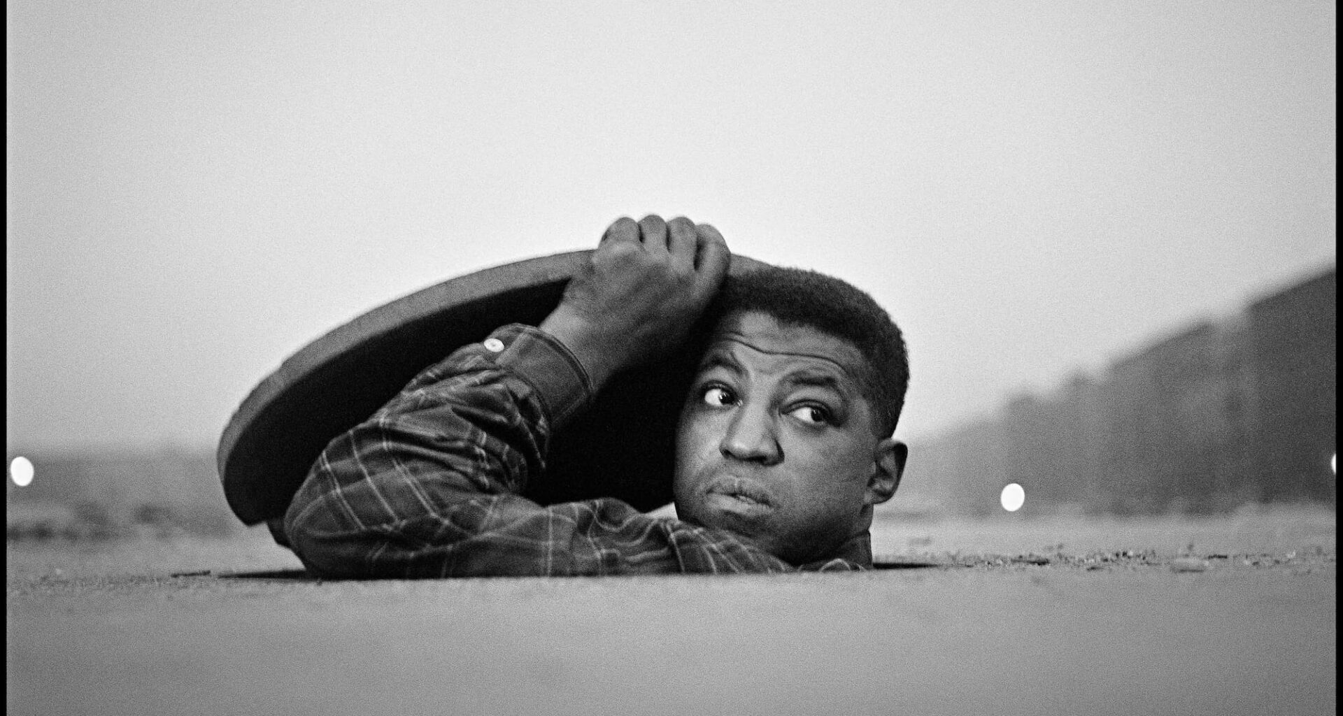 a black-and-white photograph by Gordon Parks of a Black man peeking out of a manhole cover