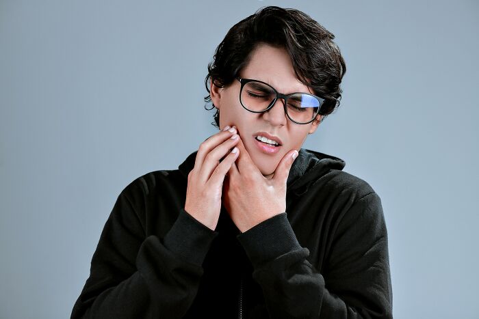 A person with glasses holding their jaw in pain, a random thing people tried for their health and it actually worked.