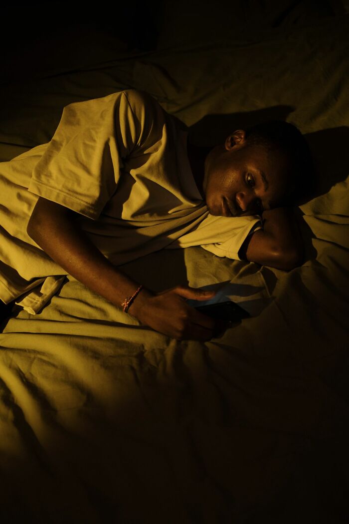 A young man in an ER bed, illuminated by a phone, representing patients in an emergency room.