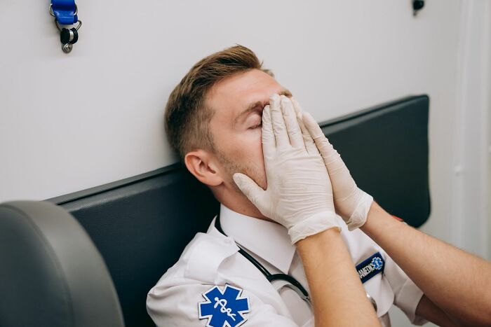 ER staff deal with ridiculous patients; a tired male paramedic covers his face with gloved hands.