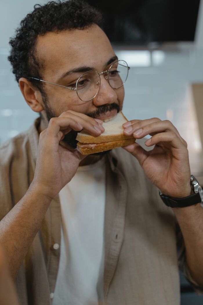 A man with glasses takes a bite of a sandwich, a scenario that might seem trivial for ER staff dealing with ridiculous patients.