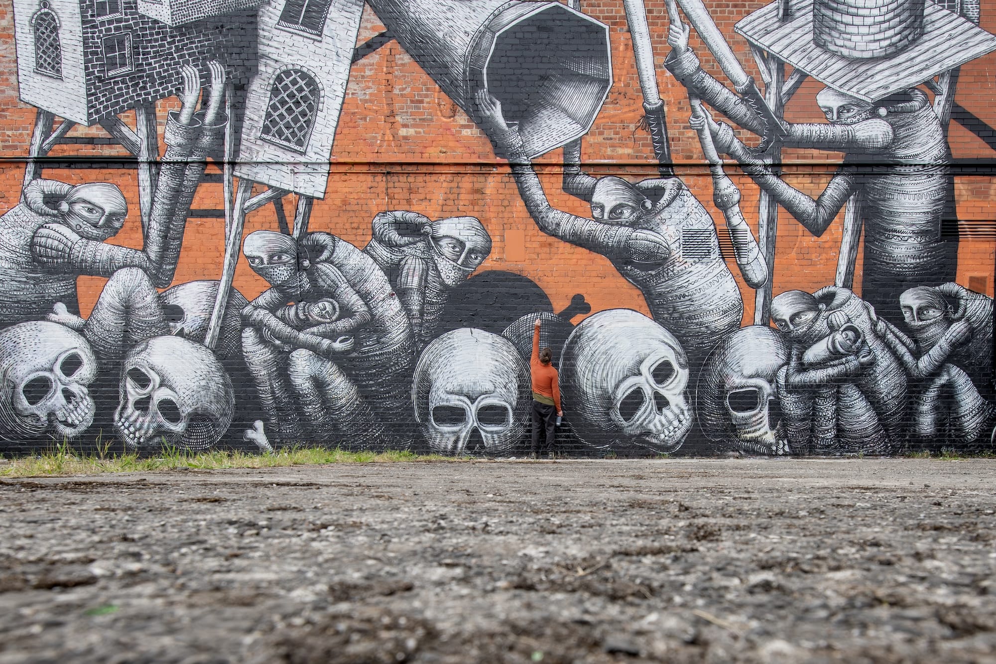 a detail of a mural by Phlegm on the side of a building featuring cartoonish figures and objects merged with lots of different shapes, including human skulls