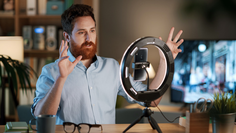 A bearded man gesturing on a video call while facing a ring light on the desk.