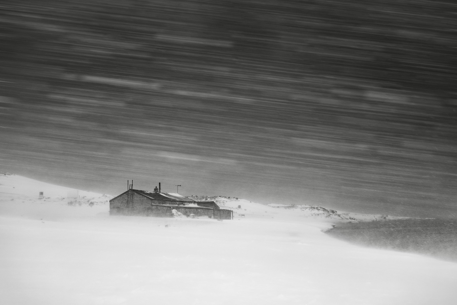 A black and white image of Captain Scott's wooden hut at Cape Evans, almost obscured by driving snow in a blizzard.