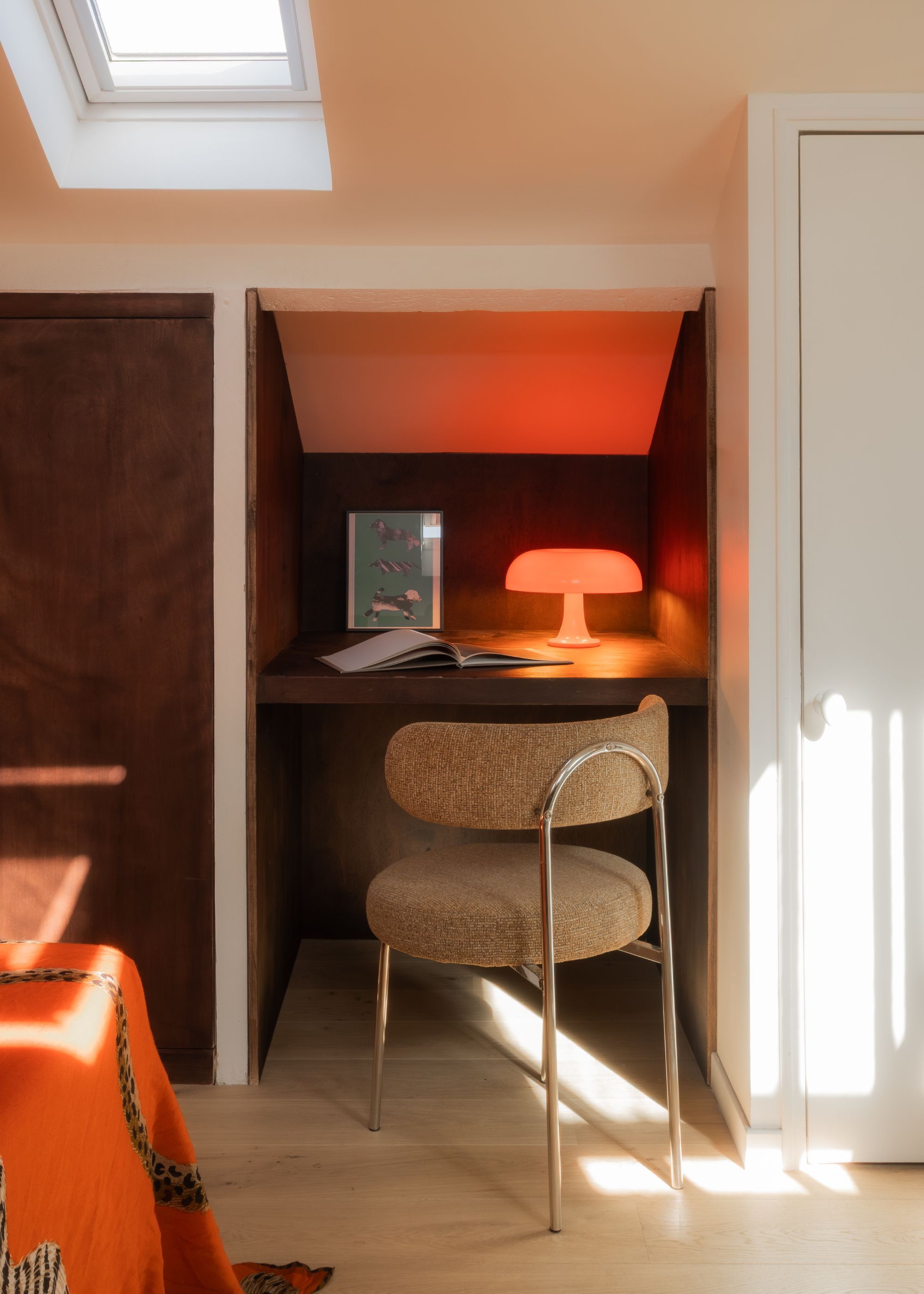 A bedroom with orange sheets, beige walls and a study hidden inside a wardrobe