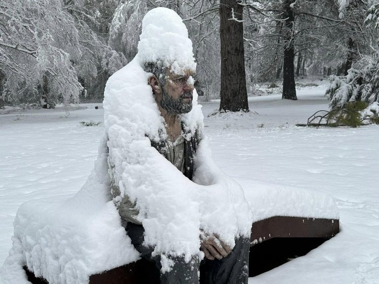 sculpture of a bearded man sitting on a bench covered in snow