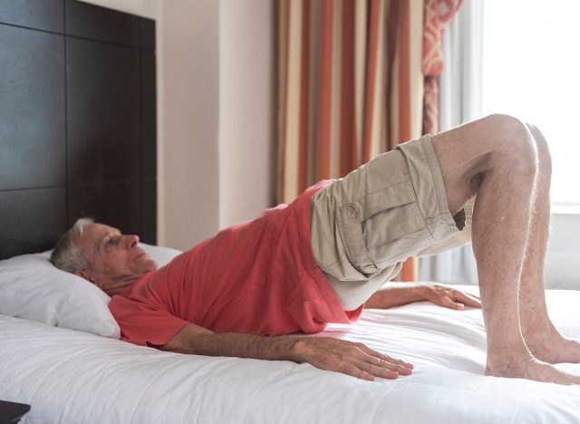 An old but fit man doing Setu Bandhasana or Bridge Pose at his hotel room. A strengthening pose for the spine and hips.