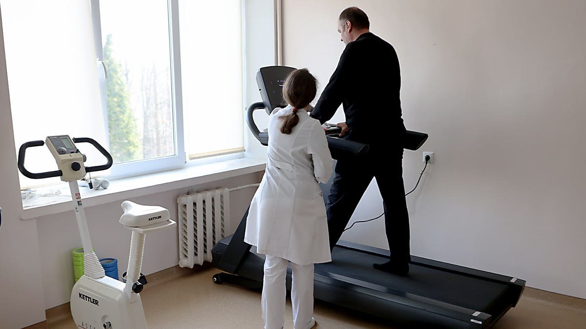 A doctor observes a man walking on a treadmill.