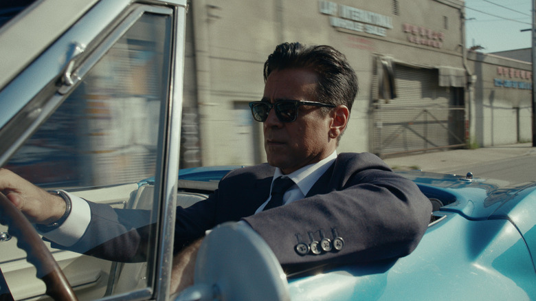 Colin Farrell as John Sugar, wearing a black suit and Ray-Ban-style sunglasses, driving an electric blue car.
