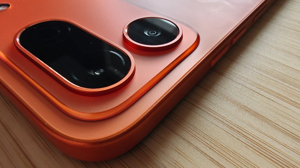 Close-up of an orange smartphone showcasing dual camera lenses with black glass covers on a wooden surface.
