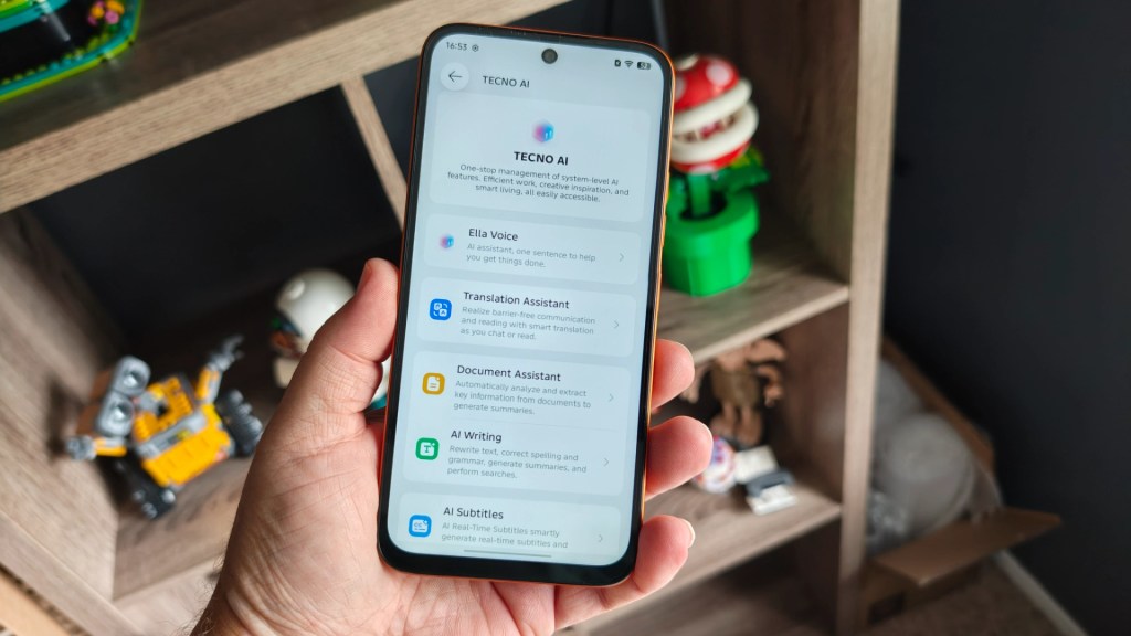 A hand holding a smartphone displaying the TECNO AI application interface, featuring various AI tools like Ella Voice and Document Assistant, on a wooden shelf with colorful toys in the background.