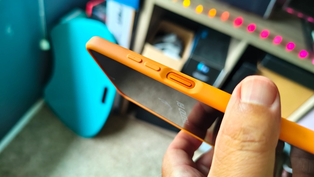 Close-up of a person holding a smartphone with an orange case, focusing on the side buttons and screen.