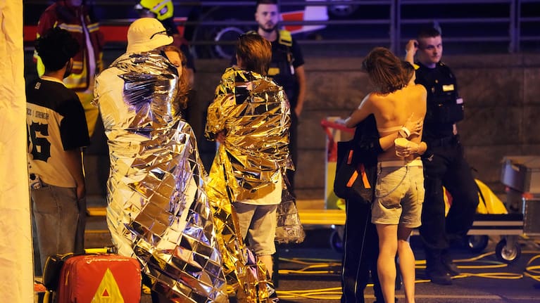 Two people embrace near others wearing thermal blankets as they stand near emergency personnel in Berlin.