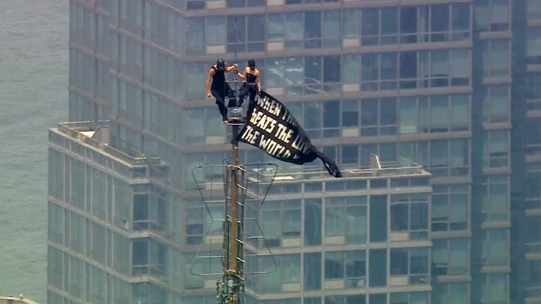 Two people stand on the tip of the antenna of the Empire State Building in New York while holding a banner on Wednesday, July 1, 2026.