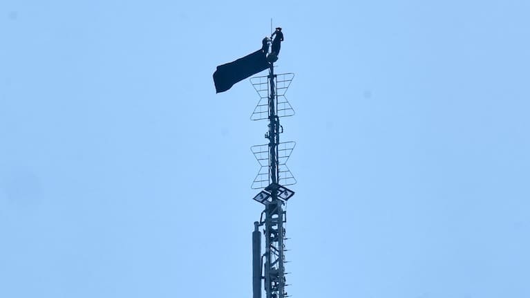 Two people stand on the tip of the antenna of the Empire State Building in New York while holding a banner.