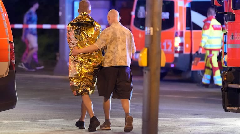 Two people walk together past emergency vehicles in Berlin, early Sunday, July 26, 2026, following the cancellation of Christopher Street Day festivities.