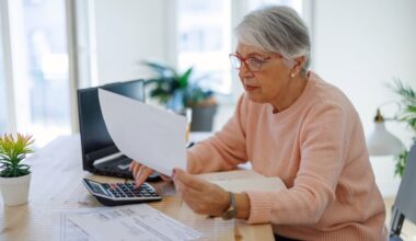 A retiree sitting at a desk is using a calculator.