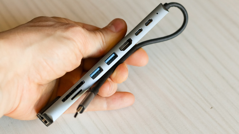 A hand holding a slim USB-C hub with multiple connectivity ports.