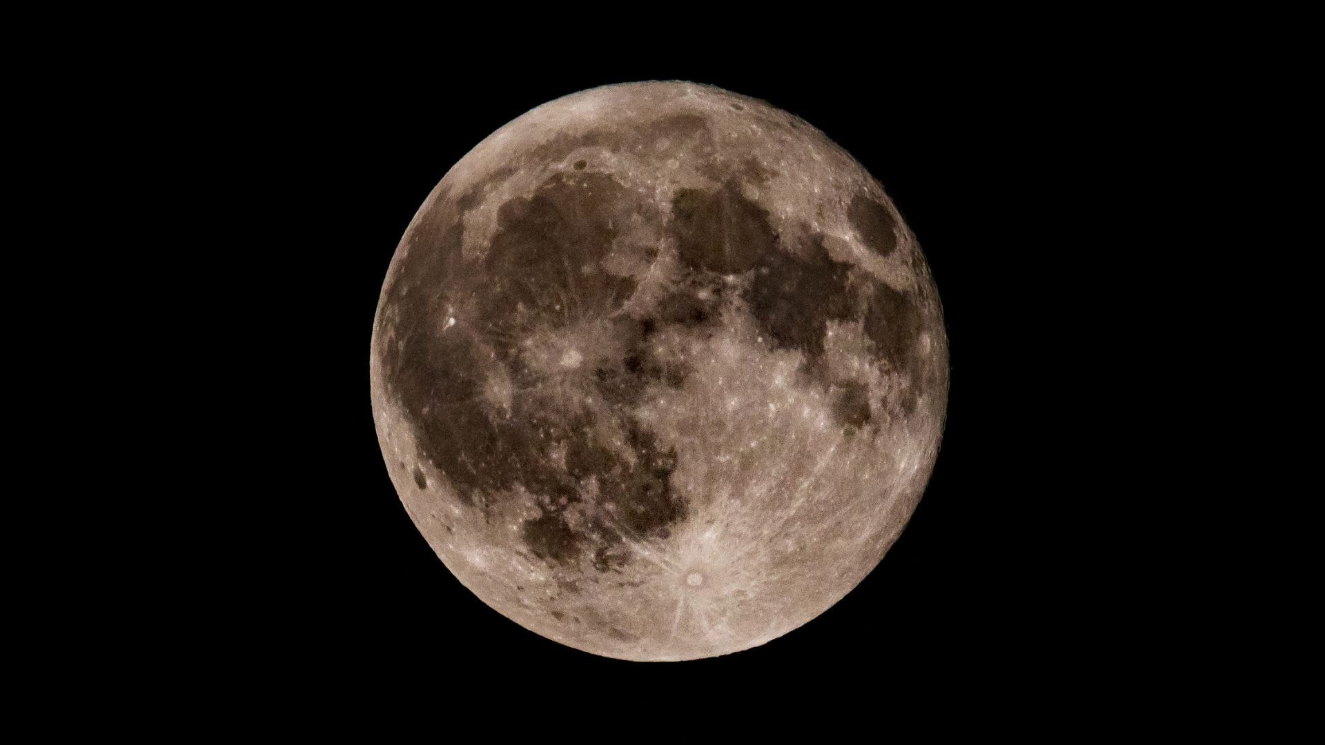 A photo of the full moon in a black sky showing dark lunar seas and bright impact craters.