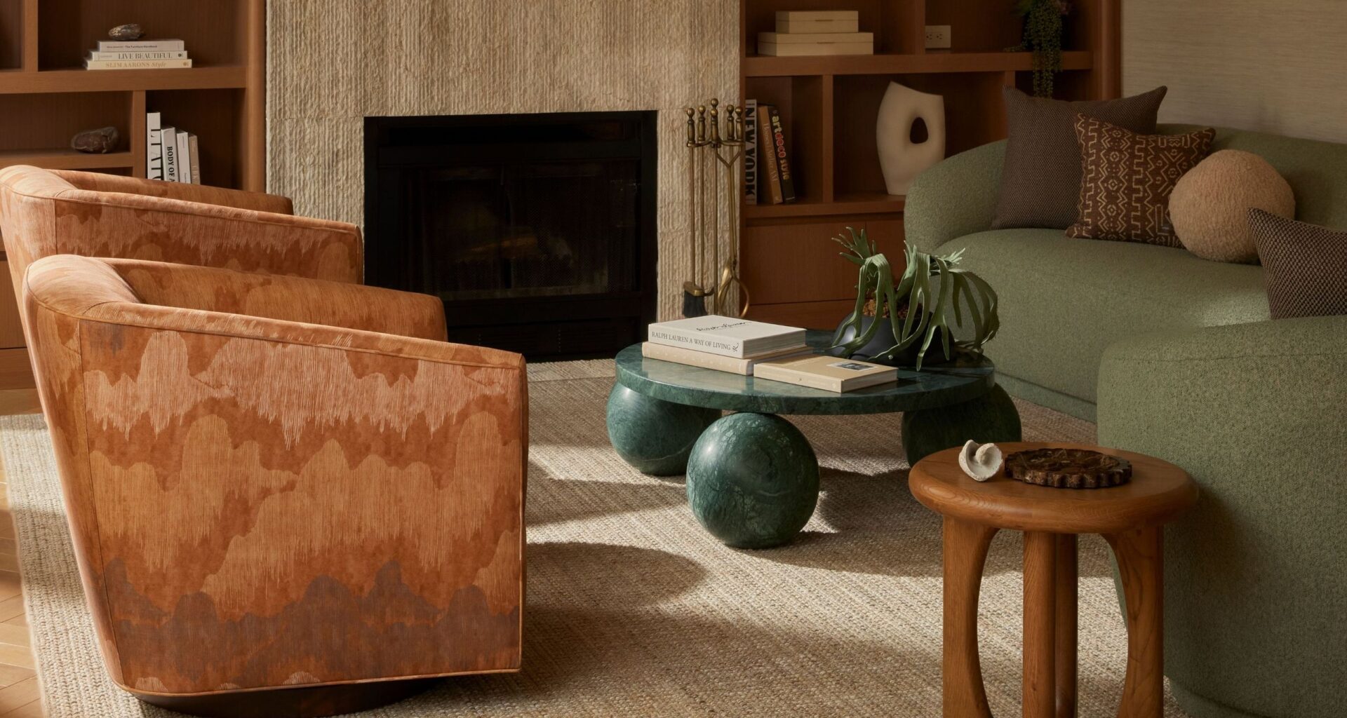 A living room with two gradient brown, velvety armchairs, a stone coffee table sitting on three petrol green spheres, a smaller one in wood, and two matching love seats in pale green.