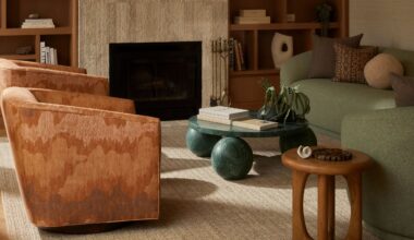 A living room with two gradient brown, velvety armchairs, a stone coffee table sitting on three petrol green spheres, a smaller one in wood, and two matching love seats in pale green.