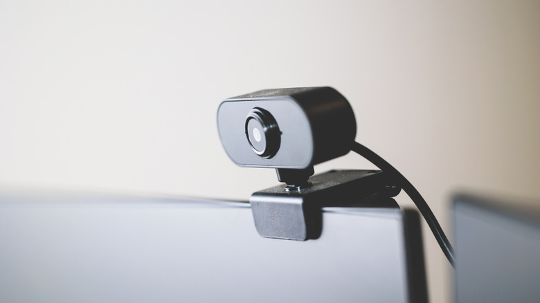 A black external webcam clipped to the top of a computer monitor.