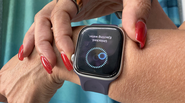 Fingers touching an Apple Watch to eject water.