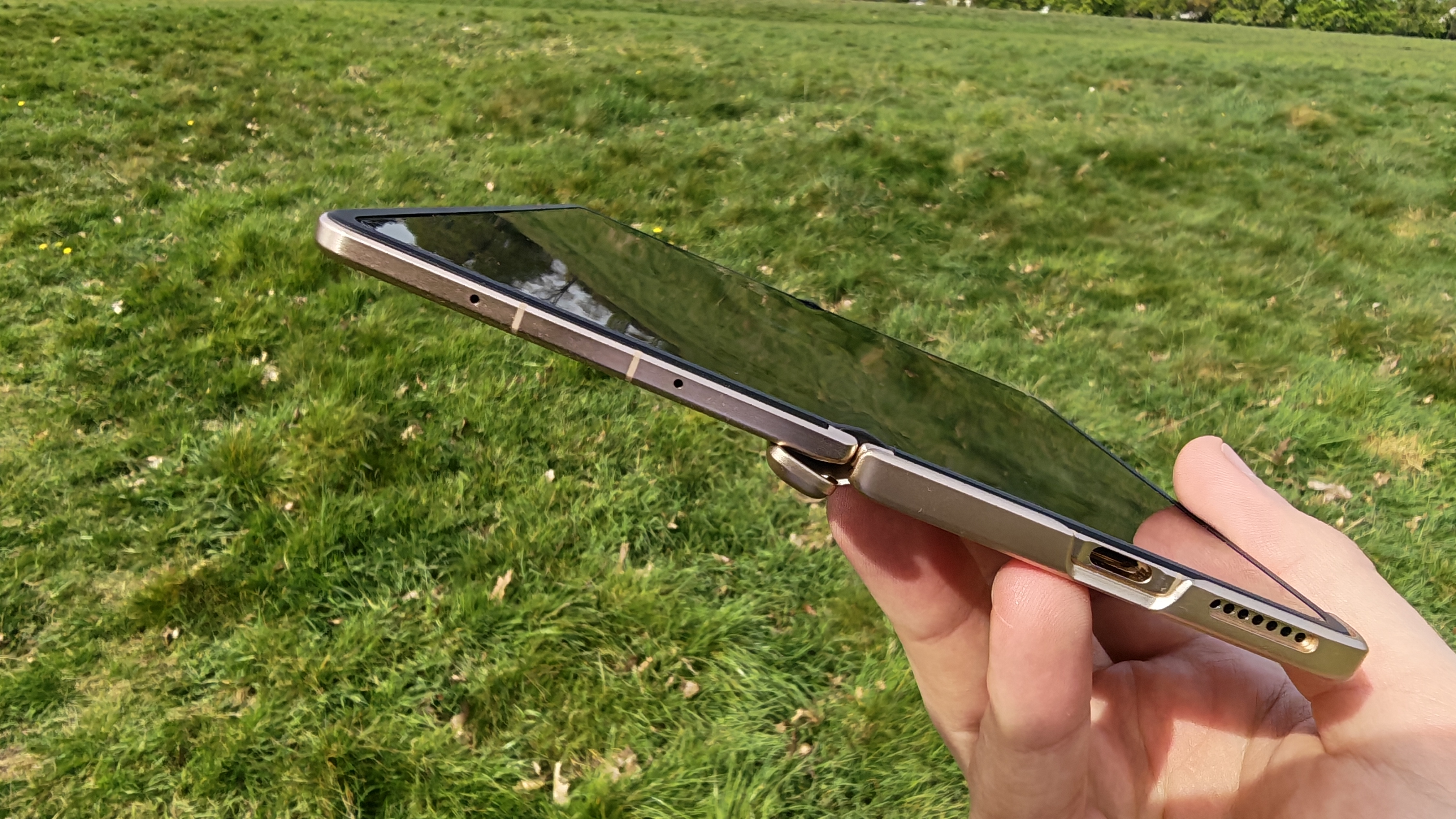 The Honor Magic V6 being held in a sunny field.