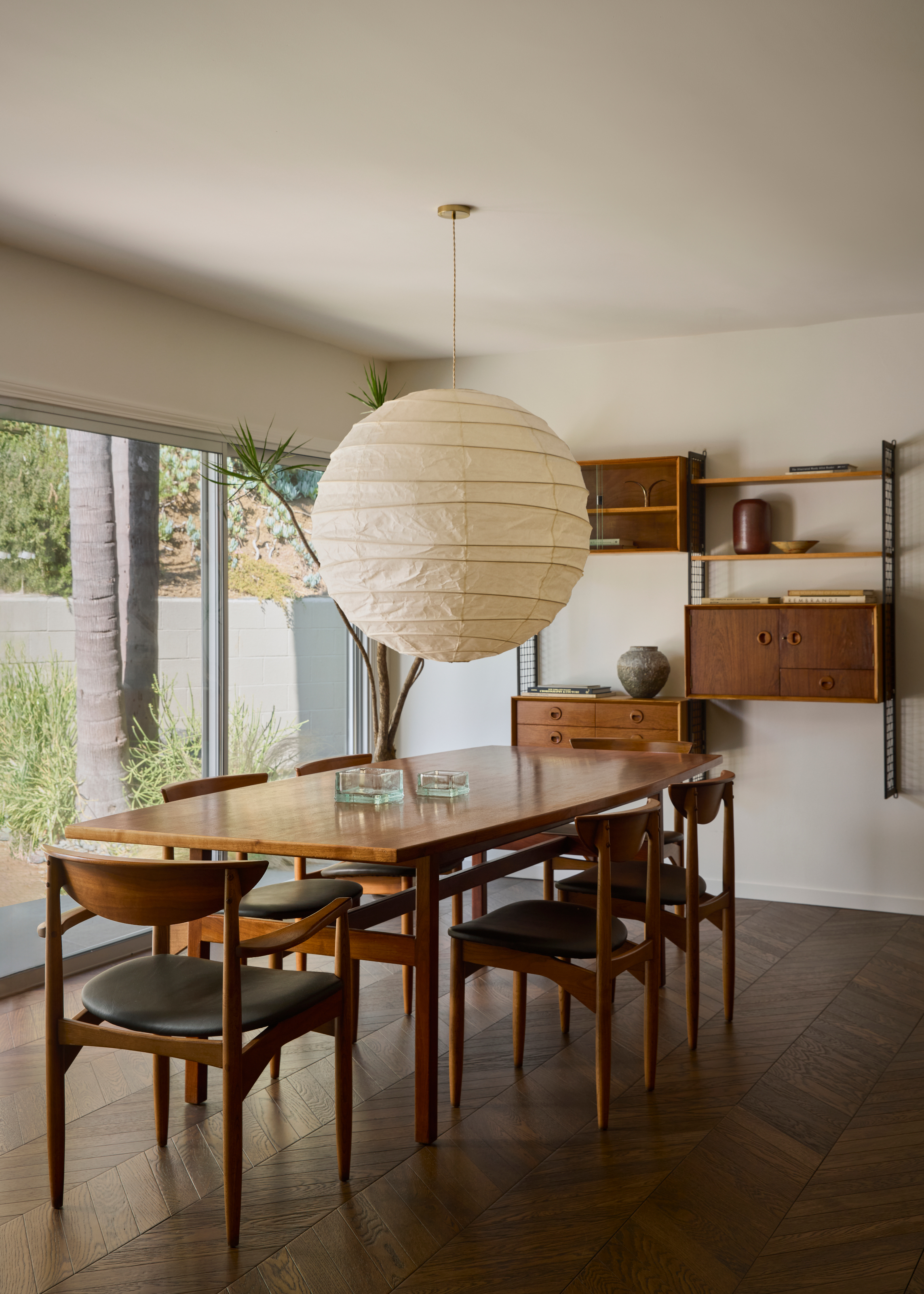 Dining room with mid-century teak dining table, teak and black chairs, paper pendant and teak mid-century wall shelves