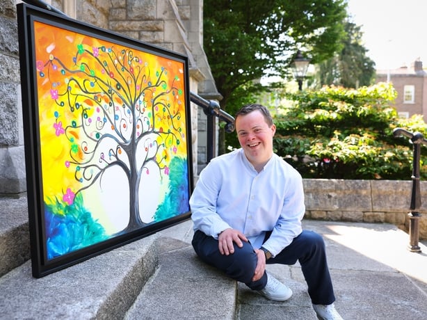 Smiling young man sits with one of his paintings on steps