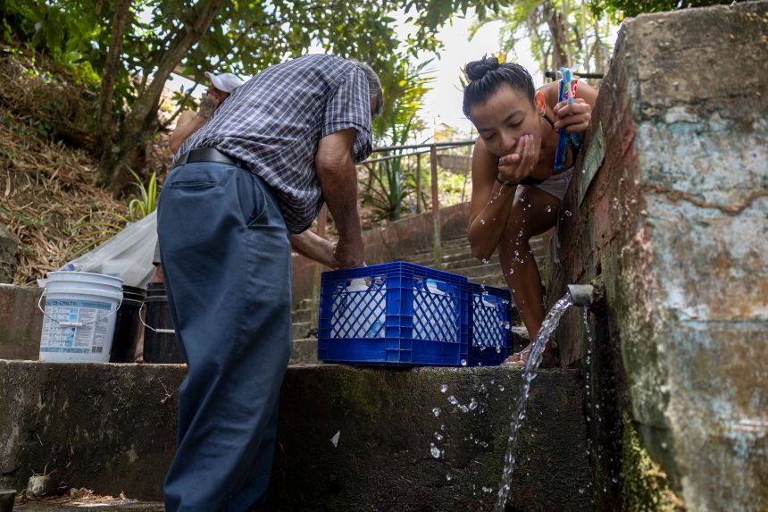 A woman uses a natural spring while brushing her teeth as residents collect water in buckets and bottles during mandatory water rationing in Trujillo Alto on August 6.