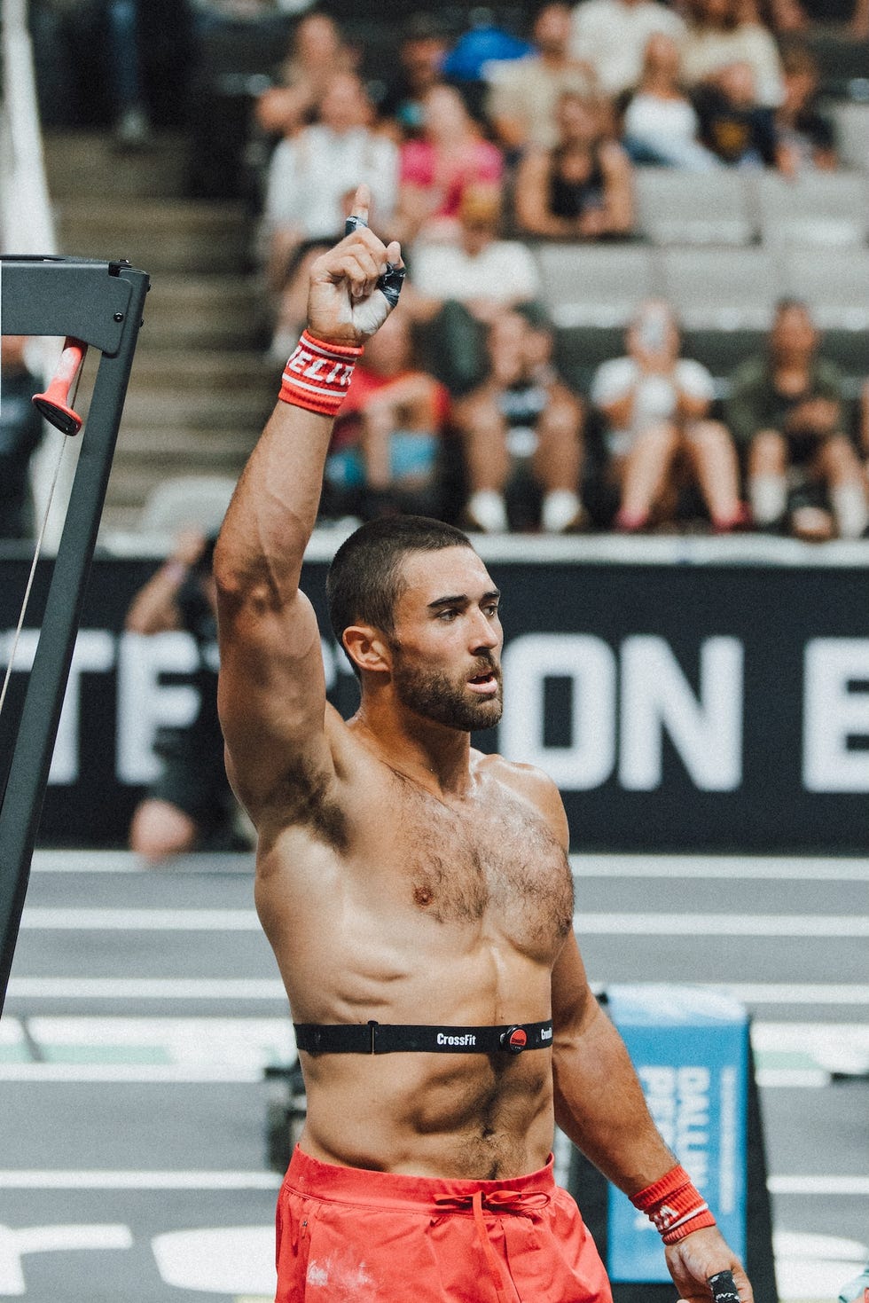 Athlete celebrating victory at a CrossFit event, wearing shorts and a heart rate monitor, with an audience in the background.