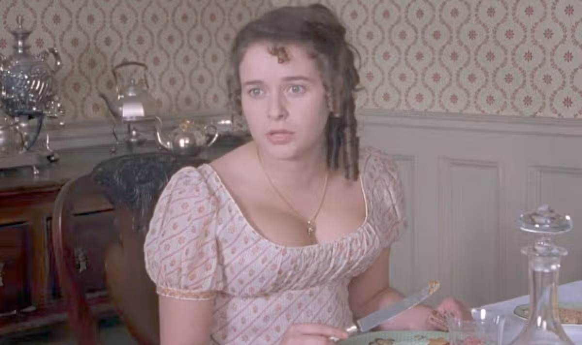 A woman in a pink dress sits at a table and looks scared