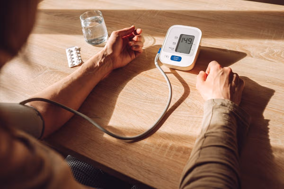 Home blood pressure check with digital monitor on wooden table and person's arm nearby