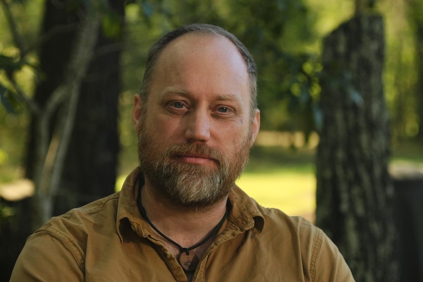 A man with an auburn beard and a beige shirt poses for camera.