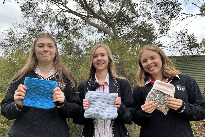 Three teenage girls in school uniforms with crocheted pouches