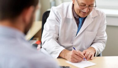 A photo of a senior male physician writing a prescription for his male patient.