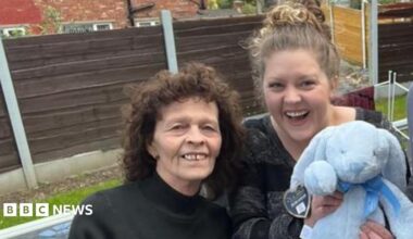 An older woman, two young women and a young man stand smiling at the camera as the young woman on the right takes a "selfie". The other young woman is holding a blue stuffed rabbit.