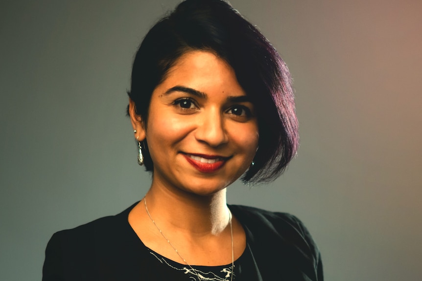 Ketvi Roopnarian stands smiling. She's wearing a patterned top and a black jacket.