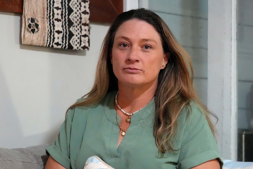 A middle-aged woman with long hair sits on a couch.