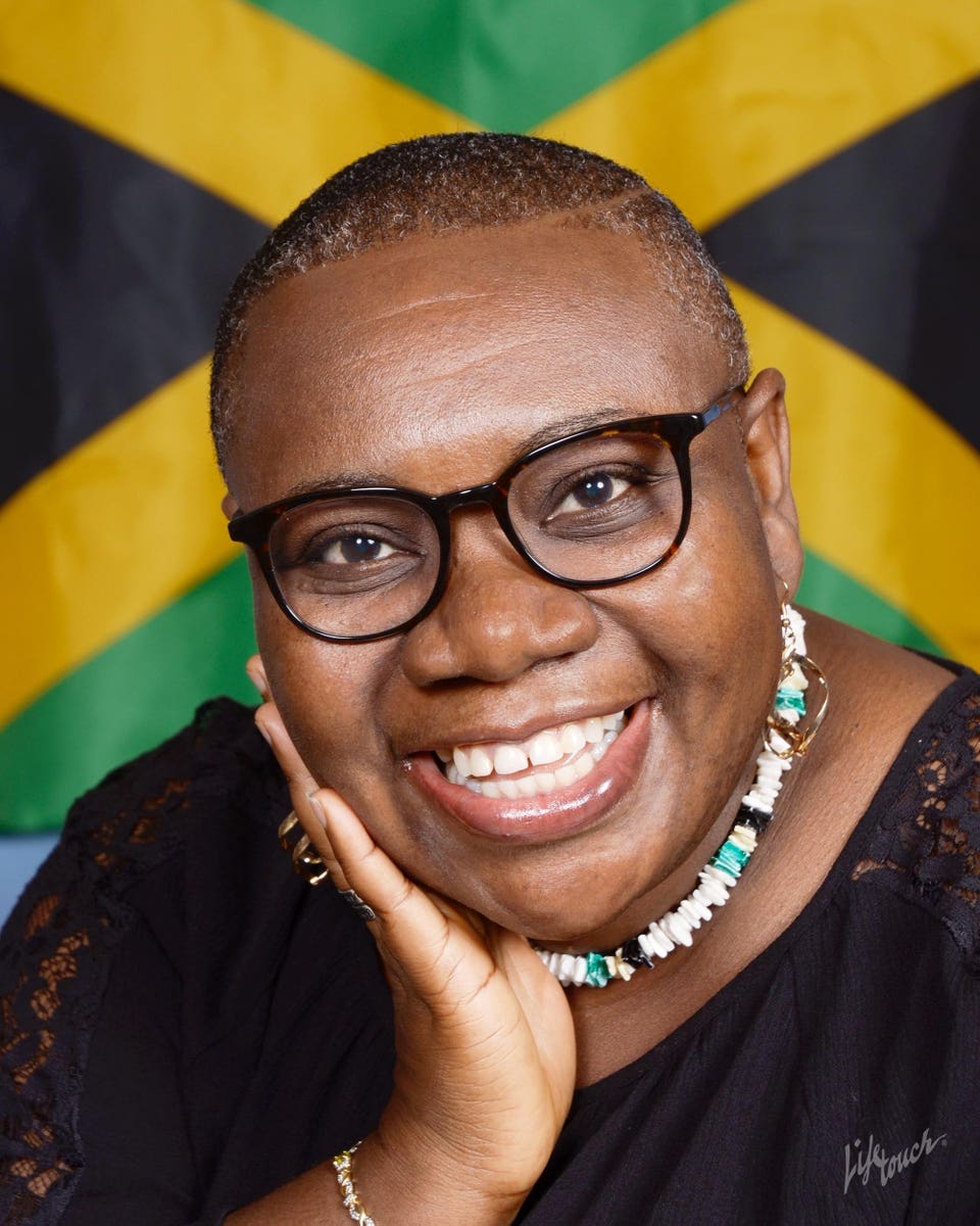 Portrait of Patricia Watson smiling in front of a Jamaican flag backdrop.