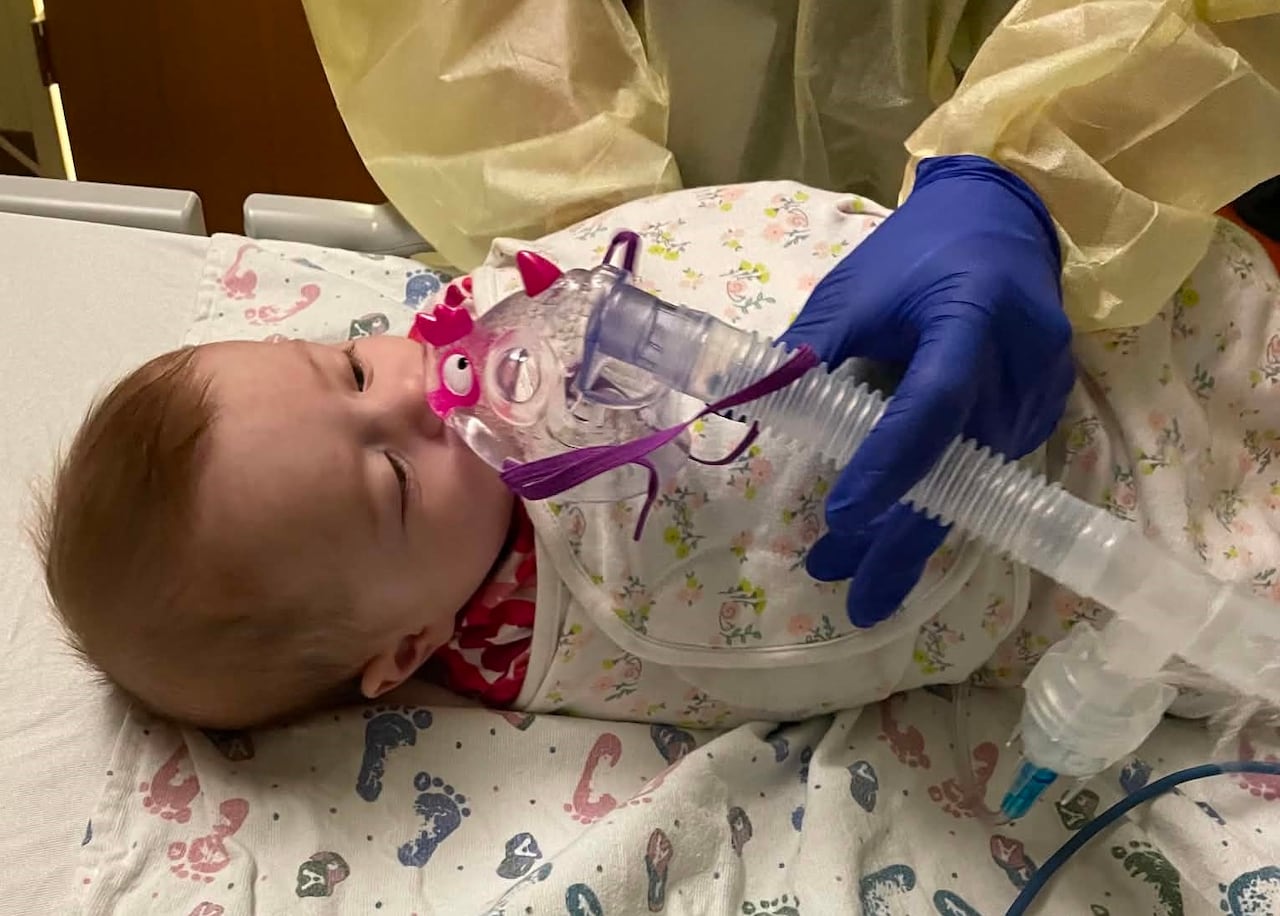 A baby breathing though a mask into a tube in a hospital.