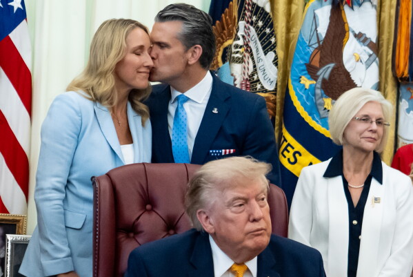 Jennifer Hegseth, left, gets a kiss from her husband Defense Secretary Pete Hegseth, as President Donald Trump concludes speaking in the Oval Office of the White House, Monday, Aug. 3, 2026, in Washington. (AP Photo/Alex Brandon)