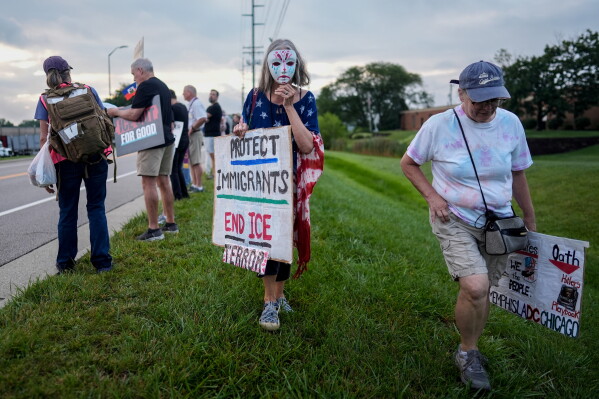 A masked protester walks with a sign during an "ICE out of Cincinnati" protest across the street from the ICE Enforcement and Removal Operations field office as Haitians who reside in Ohio arrive for appointments in Cincinnati, Sunday, Aug. 2, 2026. (AP Photo/Carolyn Kaster)