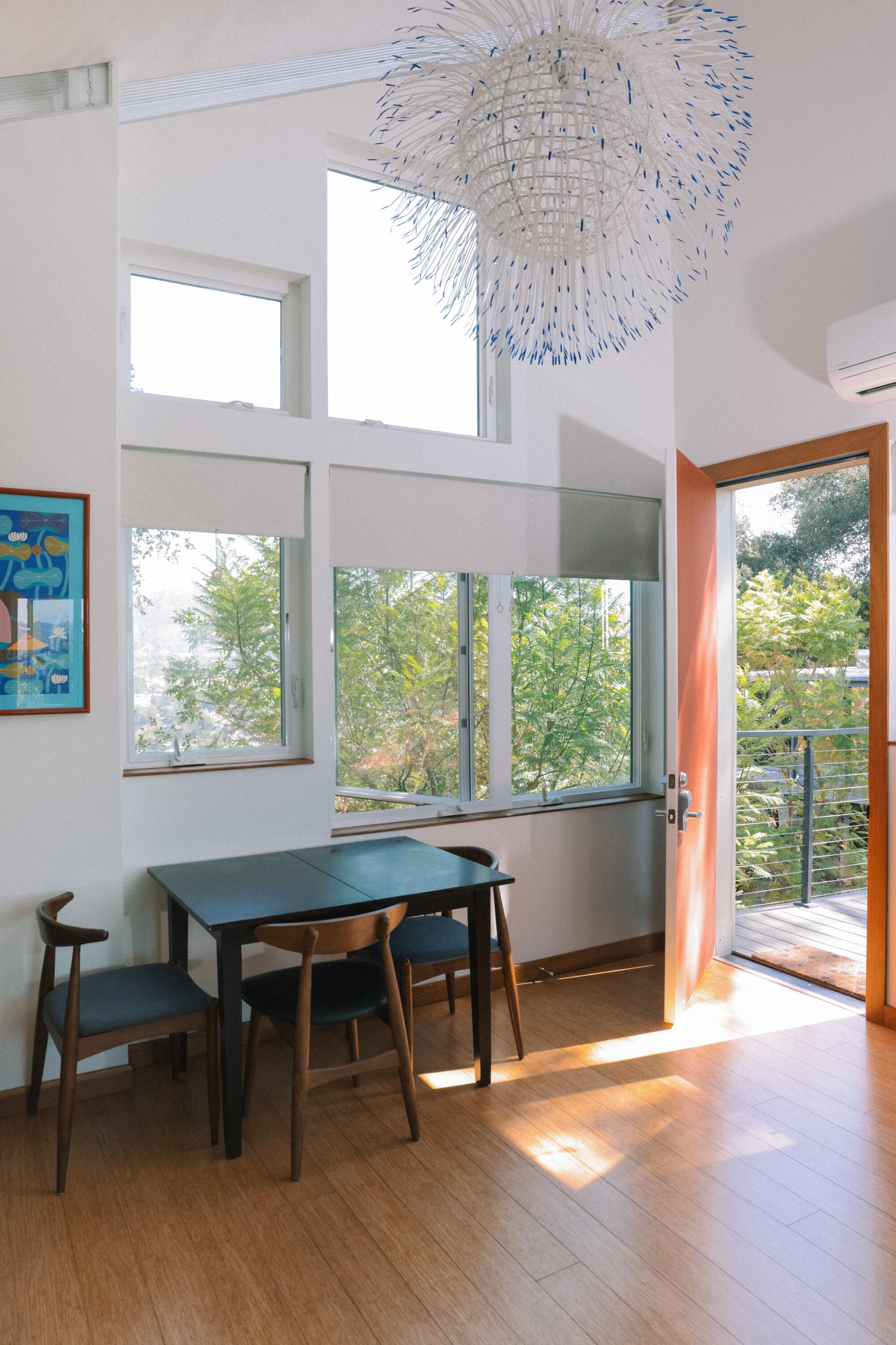 A small dining room table rests next to a group of windows and an open door 