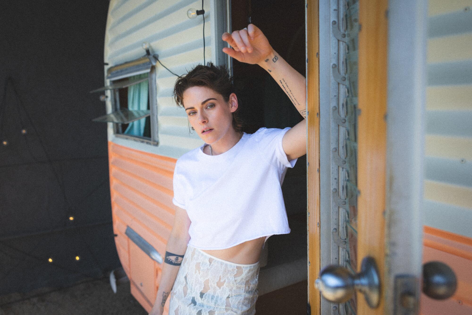 A woman stands in a doorway in a white T-shirt and lacy skirt.