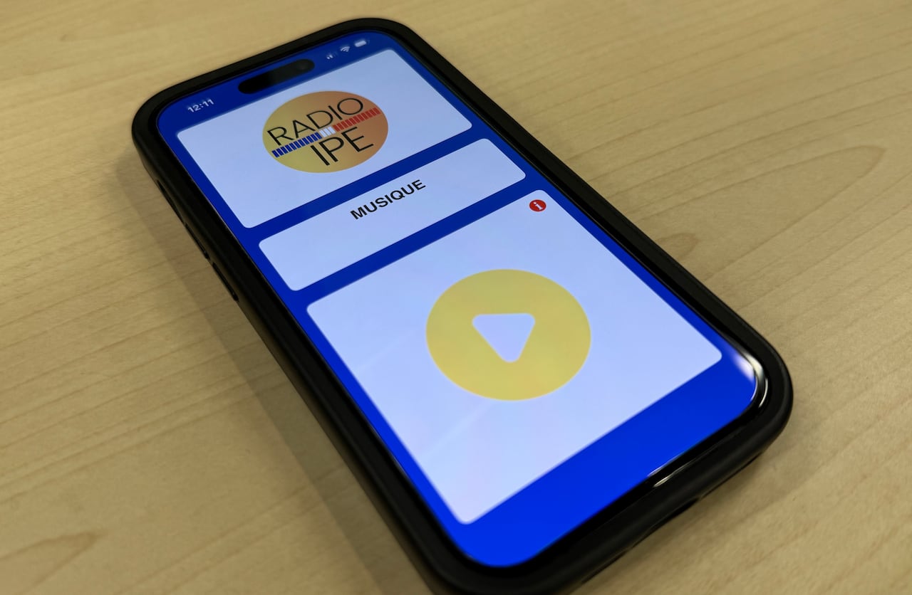 A smartphone lying on a wooden table displaying the Radio ÎPÉ mobile app interface with a yellow play button.